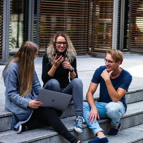 Three citizens sitting on steps discussing a city decision, one of them showing a laptop